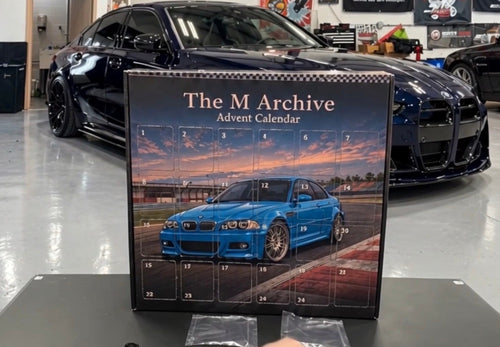 The M Archive Advent Calendar box in a garage with performance cars behind it
